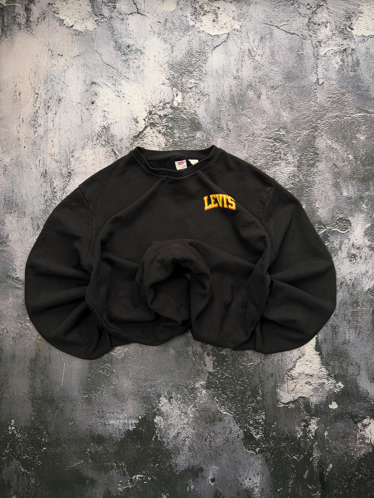 Czarna bluza Levi’s z żółtym logo, ułożona na wprost z podwiniętymi rękawami i dołem